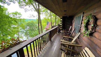 A front porch with a wooden railing, two rocking chairs, and a view of a forested area.