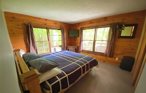 A bedroom with a king-sized bed, wooden walls, a small table, and a window with curtains.