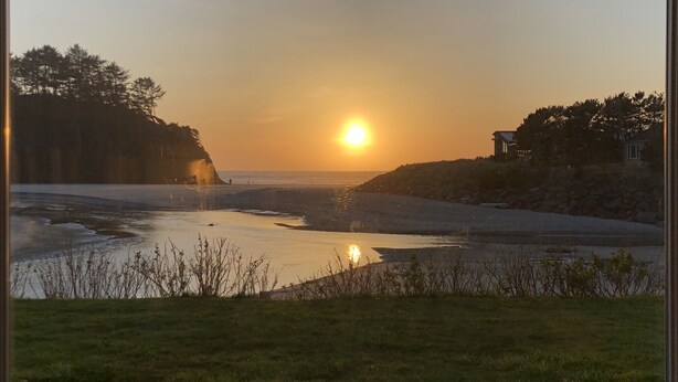 A sunset view from a grassy area with two Adirondack chairs facing a body of water and a distant shoreline. - Prime Ocean/Beach Location & Spectacular View!Ground Level Condo,Fresh Update (Neskowin)