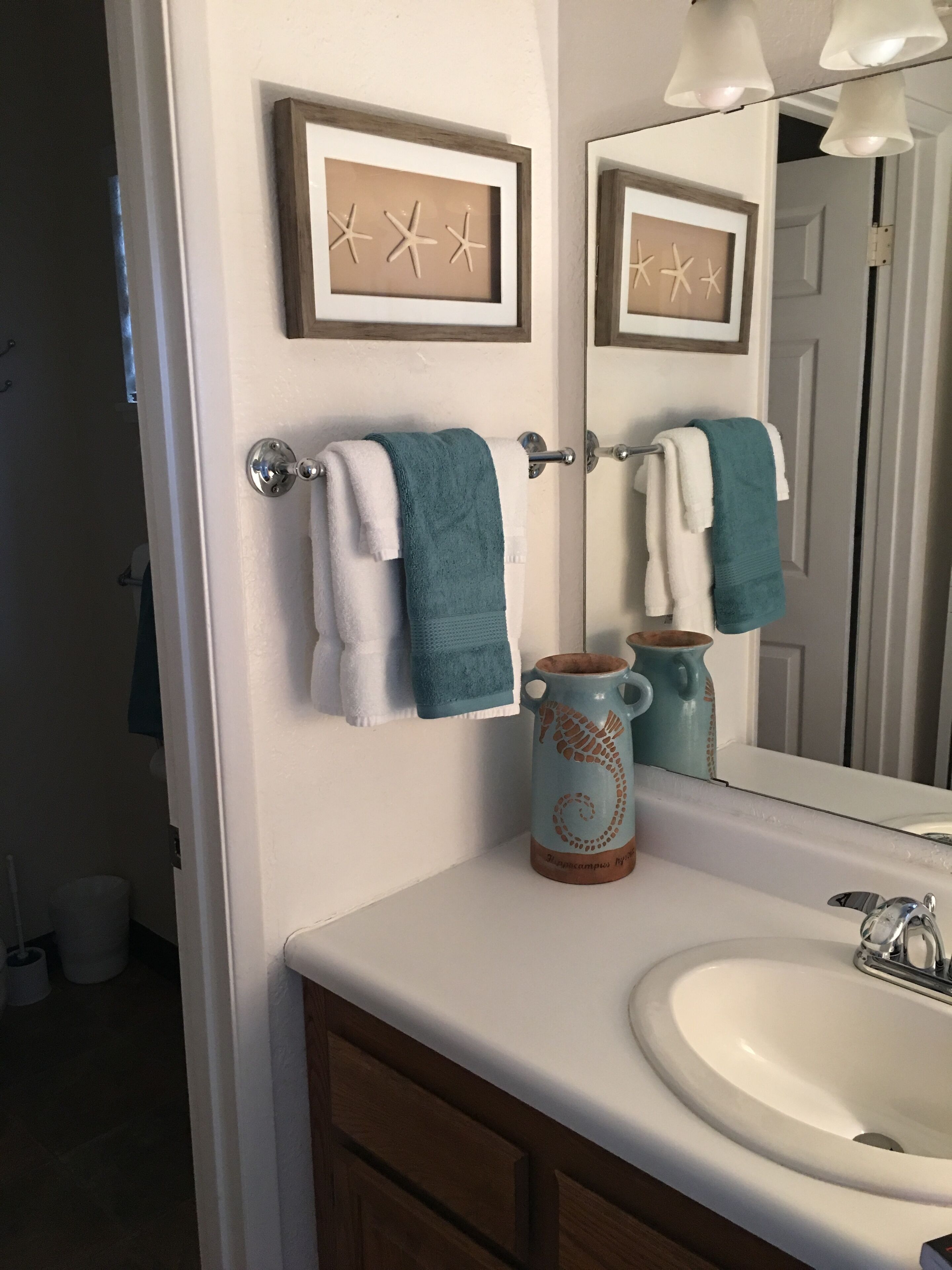 Une salle de bain avec un lavabo blanc, un miroir et deux décorations en forme d’étoiles de mer encadrées accrochées au mur.