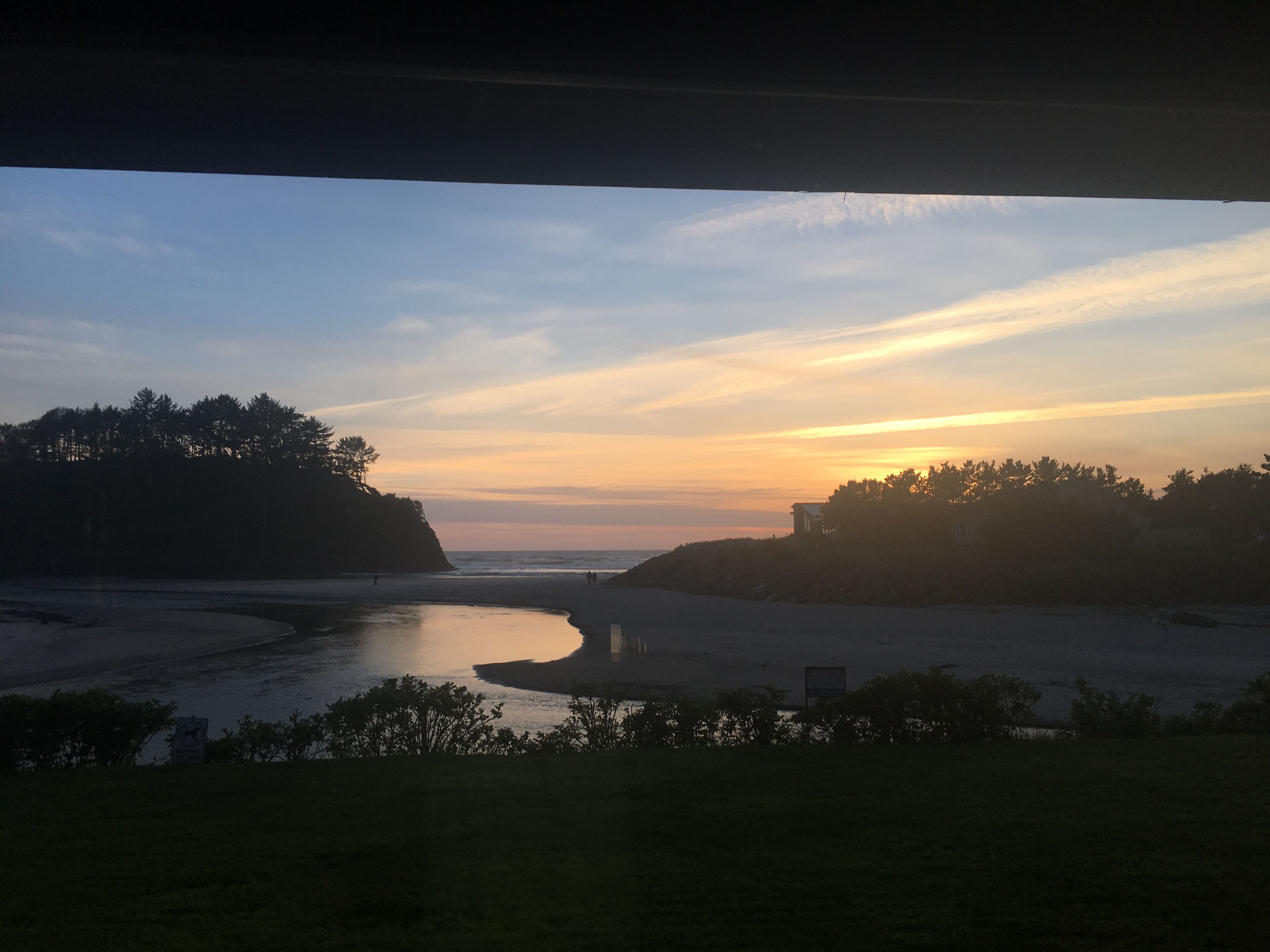 A coastal landscape with a calm river, trees, and a distant shoreline.