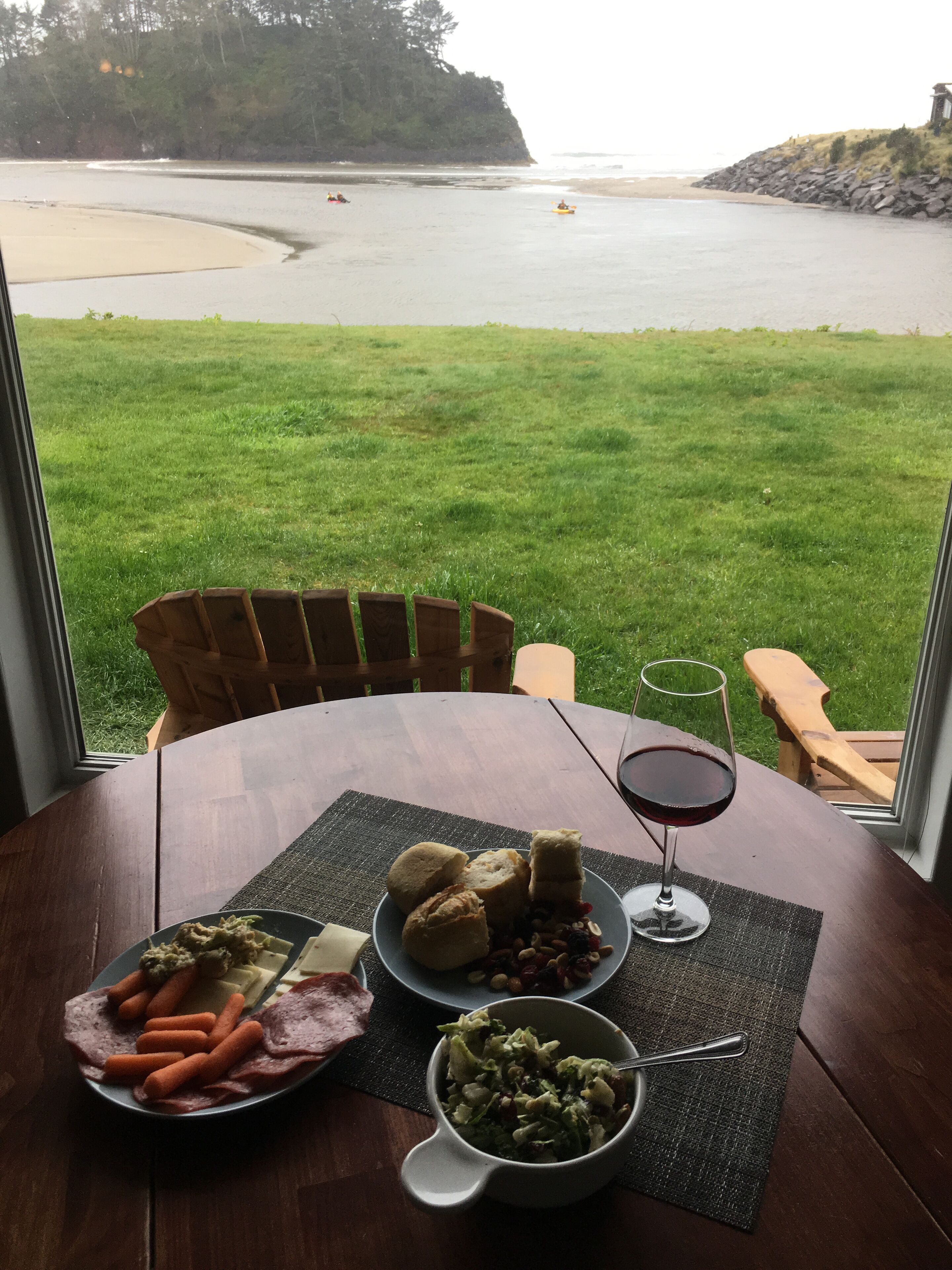 A table with food and drink, overlooking a beach and grassy area.