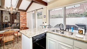 A kitchen with granite countertops, a dishwasher, and a large window with a view of a patio.