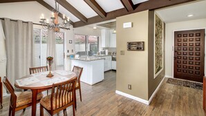 A spacious kitchen with a central island, wooden dining table with chairs, and a chandelier.