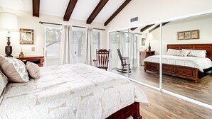 A bedroom with a large bed, wooden beams on the ceiling, a chair, and a large mirror.