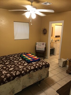 Relax in this serene bedroom with a large bed and ceiling fan, featuring a door to a bathroom with a sink and mirror.