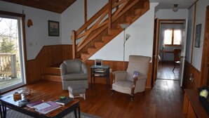 Amplia sala de estar con una escalera de madera, un sofá, una silla y una mesa de centro con varios objetos.