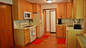 Cocina compacta con armarios de madera, microondas, refrigerador, estufa y cafetera.