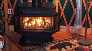 Una estufa de leña con fuego a la vista, frente a un muro de celosía con cortina y una lámpara con diseño de alce.
