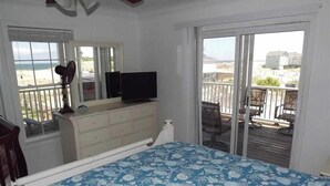 Une chambre avec un lit, une commode, une télévision et un balcon donnant sur la plage.