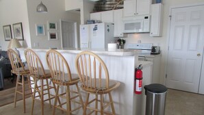 A kitchen with a white countertop, wooden chairs, a stainless steel trash can, and a fire extinguisher. - Enjoy an uncrowded beach, but close to shopping and restaurants. (Surf City)
