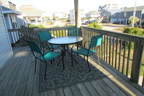 A wooden deck with a round table and four chairs, overlooking a residential area with houses and parked cars.
