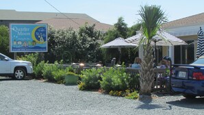 A restaurant with outdoor seating, a signboard advertising 'Quarter Moon', and a parking area with cars. - Enjoy an uncrowded beach, but close to shopping and restaurants. (Surf City)