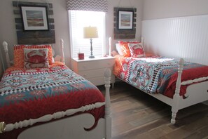 A bedroom with two beds, a nightstand, a lamp, and two framed pictures on the wall.