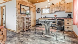 A rustic kitchen with wooden cabinets, a dining table, and a coffee machine. - Romantic Lakeview Treehouse with Jacuzzi Tub & Private Deck (Stigler)