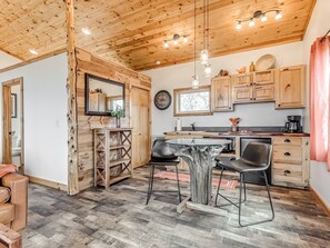 A rustic kitchen with wooden cabinets, a dining table, and a coffee machine. - Romantic Lakeview Treehouse with Jacuzzi Tub & Private Deck (Stigler)