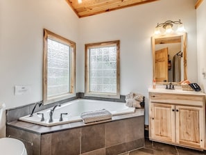 Une salle de bain avec une baignoire sur pieds, un meuble-lavabo avec un miroir et deux fenêtres.