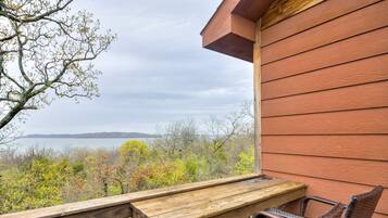 A wooden deck with a table and wicker chairs overlooking a body of water and trees.