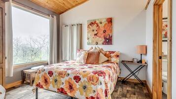 A bedroom with a bed, a window, a painting, and a bedside table.