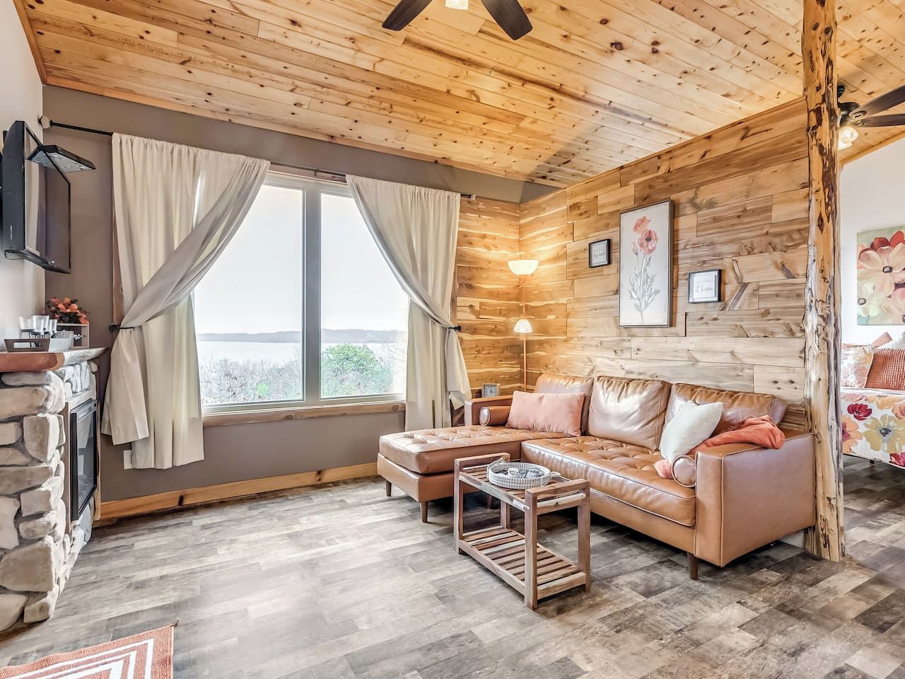 Un cuarto acogedor con techo de madera, chimenea de piedra, un sofá y un ventanal con cortinas.