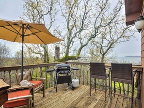Una terraza de madera con una parrilla, sillas y una sombrilla.