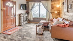 A cozy living room with a fireplace, a sofa, a coffee table, and a television mounted on the wall.