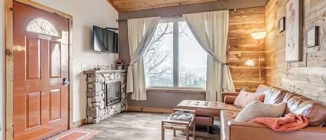 Una sala de estar acogedora con chimenea, un sofá, una mesa de centro y un televisor montado en la pared.