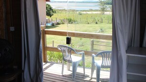A room with a bed, a wooden deck, and a view of a lake and fields. - Casa Abacate (Imbituba)
