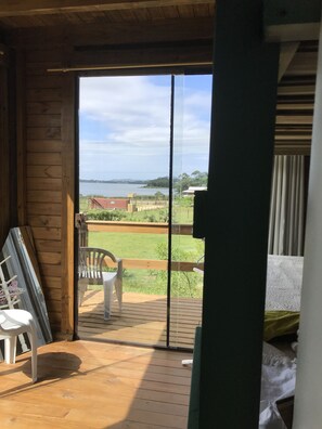A room with a wooden floor, a sliding glass door leading to an outdoor deck with a chair and a table. - Casa Abacate (Imbituba)