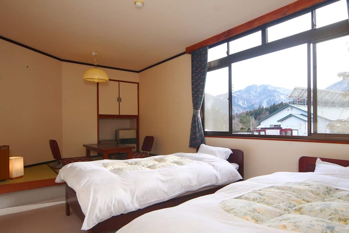 Ett hotellrum med två sängar, ett skrivbord, en stol och ett stort fönster med utsikt över bergen.