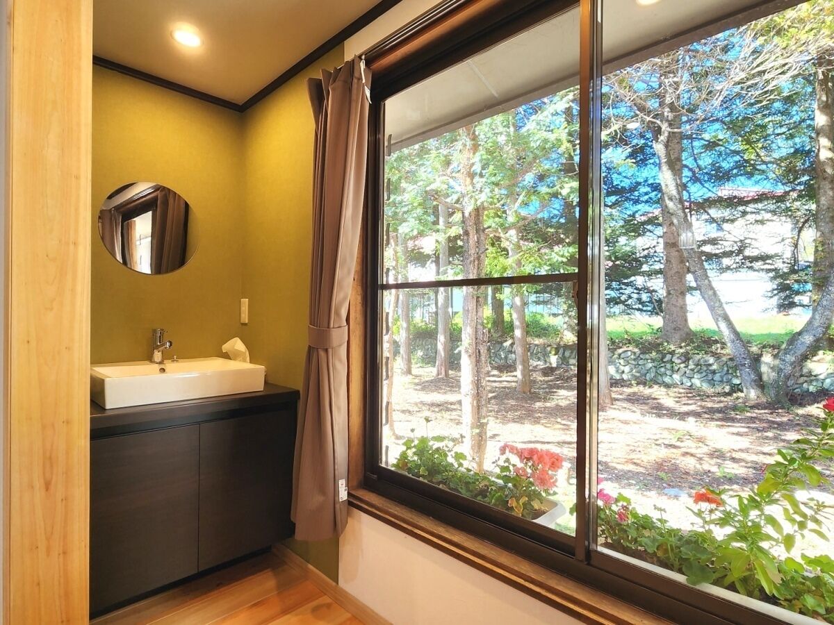 Un baño con lavamanos, espejo y ventana con vistas a un jardín.