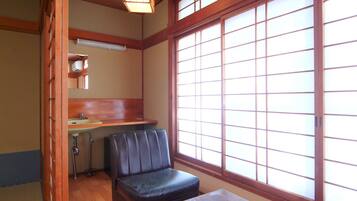 Una habitación japonesa tradicional con suelo de tatami, una mesa de madera baja, un banco acolchado, un lavabo pequeño y una ventana con marcos de madera.