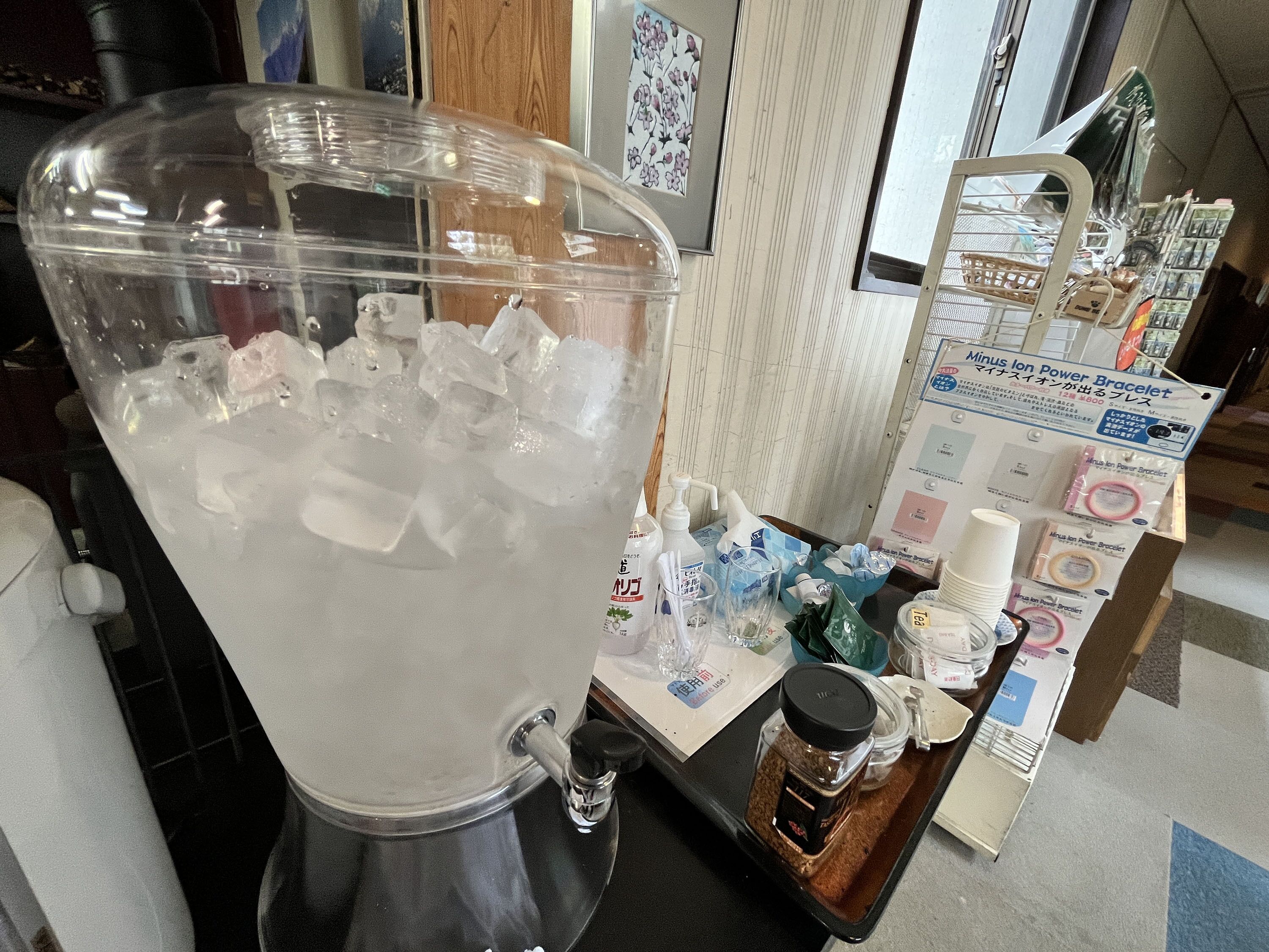 A beverage dispenser filled with ice and water, a small table with various items including a bottle of tea, and a display of products like a power bracelet.