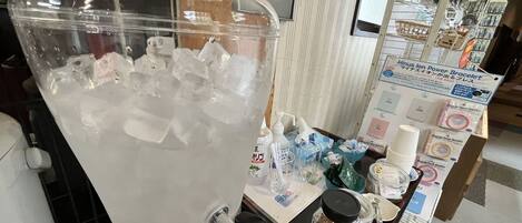 A beverage dispenser filled with ice and water, a small table with various items including a bottle of tea, and a display of products like a power bracelet.