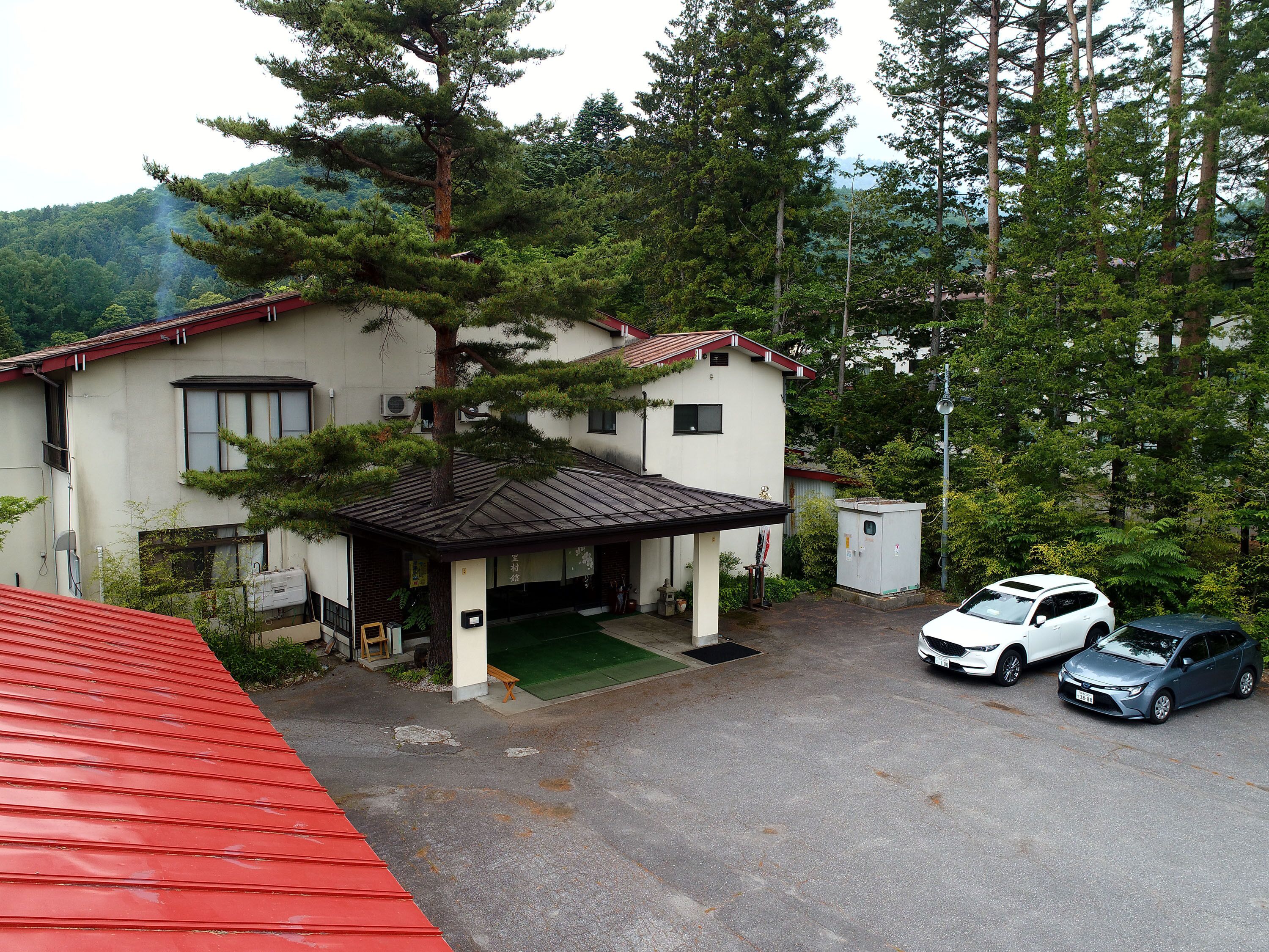 A two-story building with a red roof, a covered parking area, and two cars parked in front.