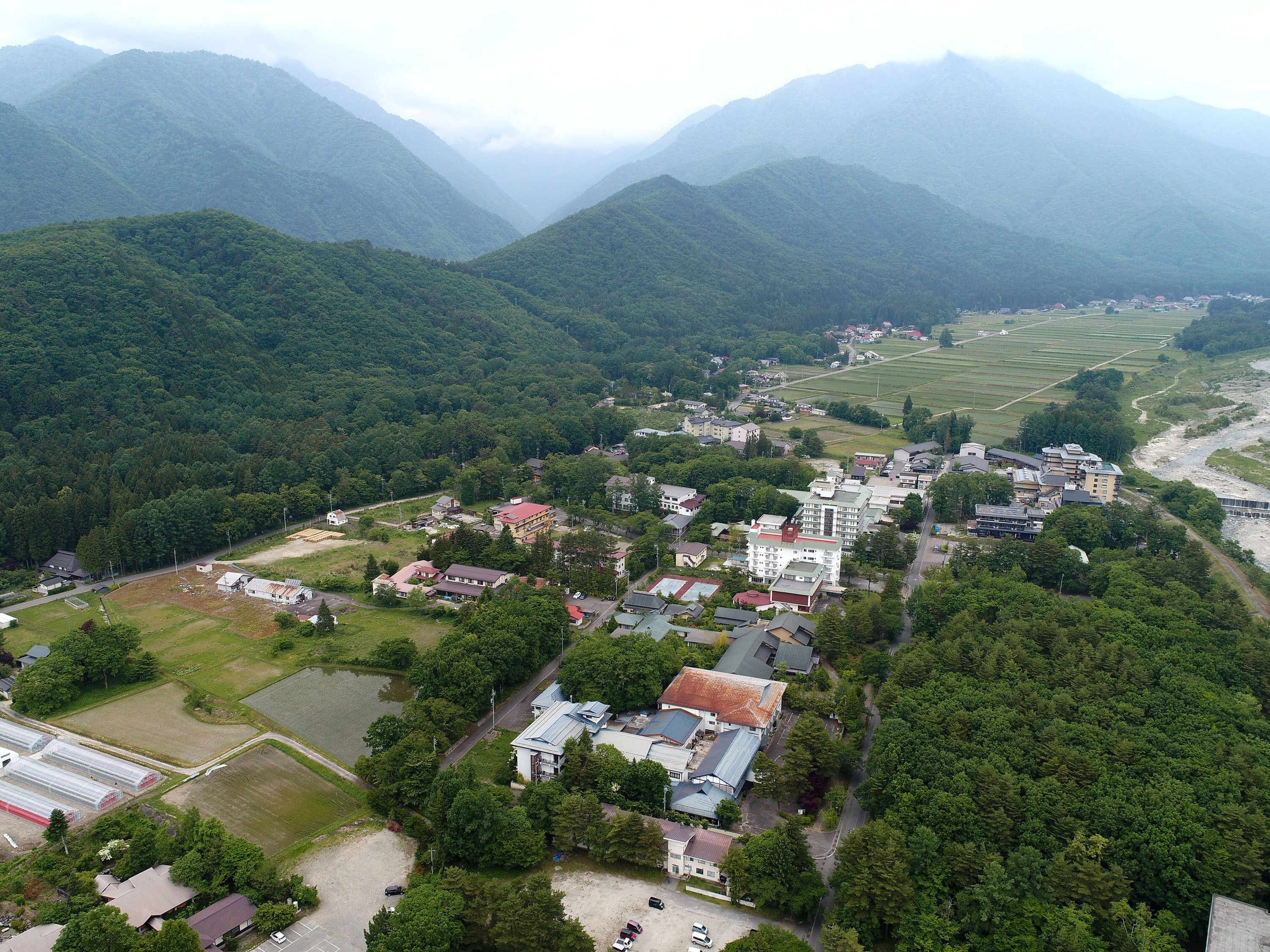 Vista aérea de uma cidade com edifícios residenciais, campos verdes e montanhas ao fundo.