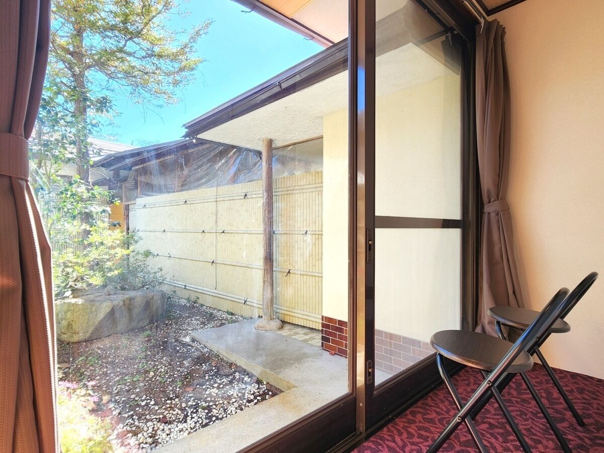 A room with a sliding glass door leading to a small outdoor area with a tiled floor and a rock. There is a folding chair in the room.