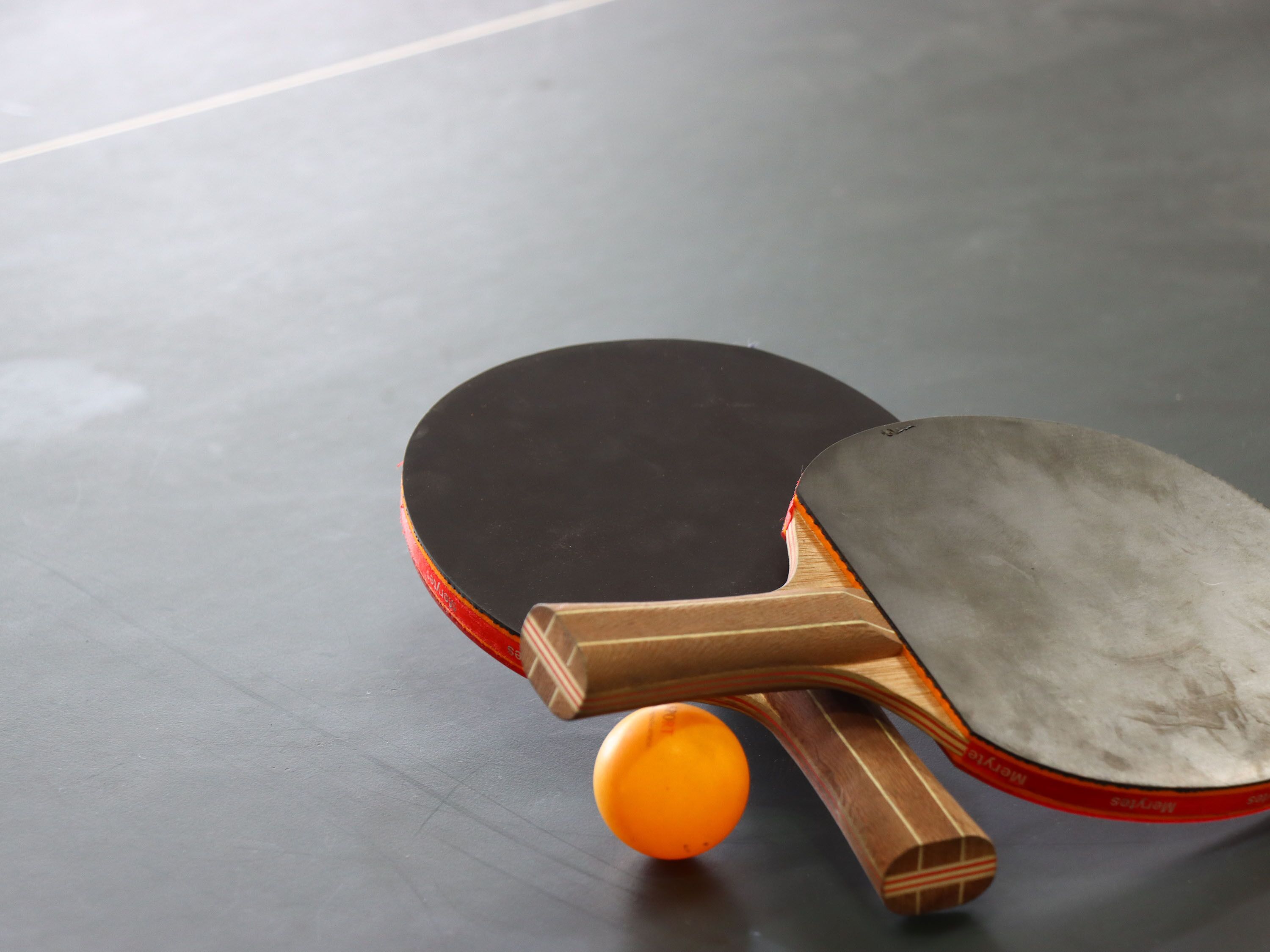 A table tennis paddle with a wooden handle and a rubberized surface, placed on a smooth, dark floor.