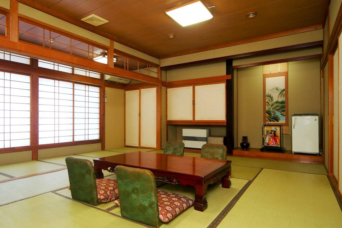 Ett traditionellt japanskt rum med tatamimattor på golvet, ett lågt träbord, gröna, vadderade stolar, skjutdörrar och en tavla på väggen.