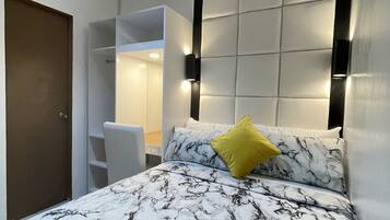 A bedroom with a bed featuring a marble-patterned bedspread, a yellow pillow, and a headboard with wall-mounted lights.