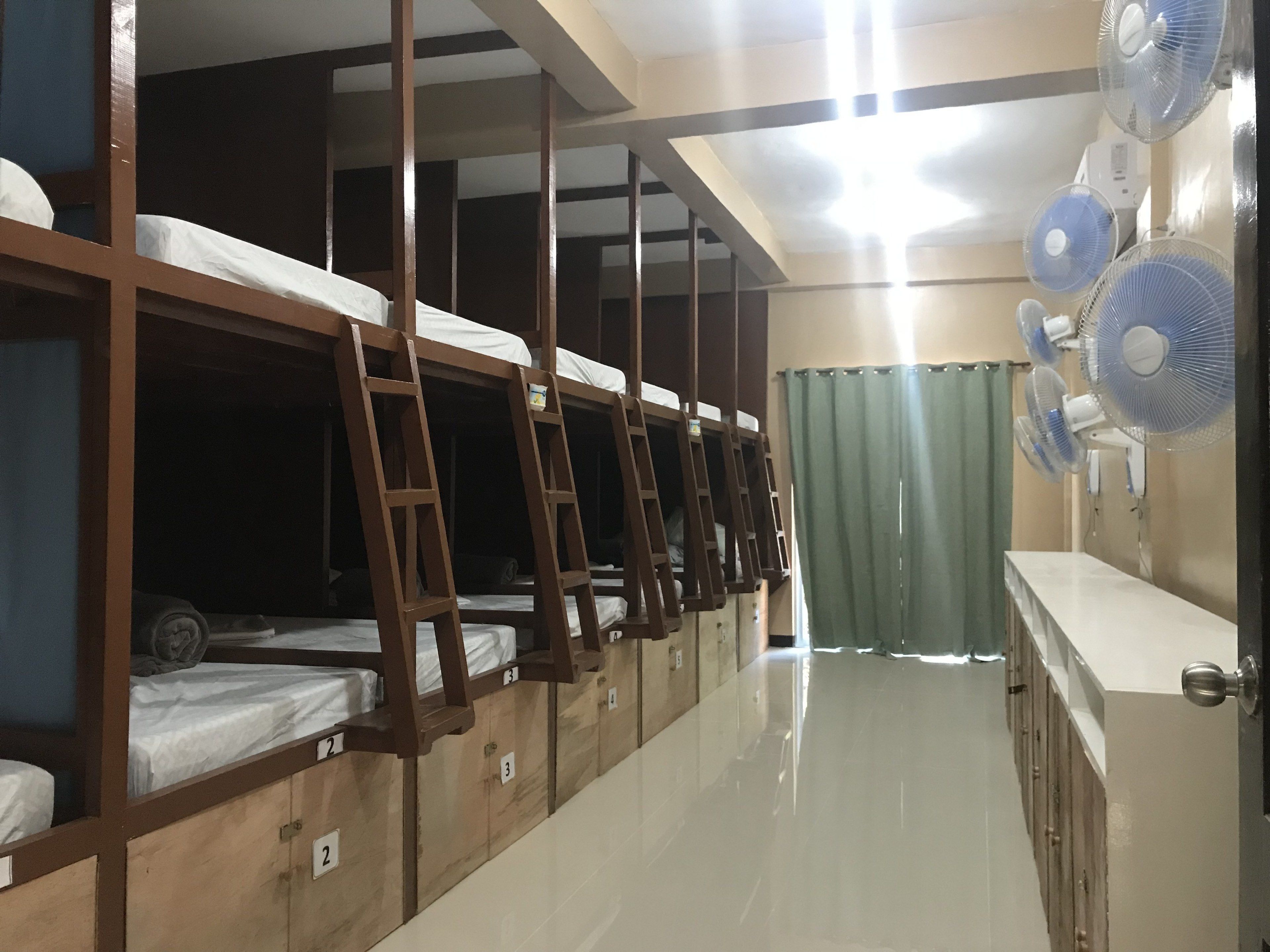 Un dormitorio con literas, un escritorio y varios ventiladores de pared.
