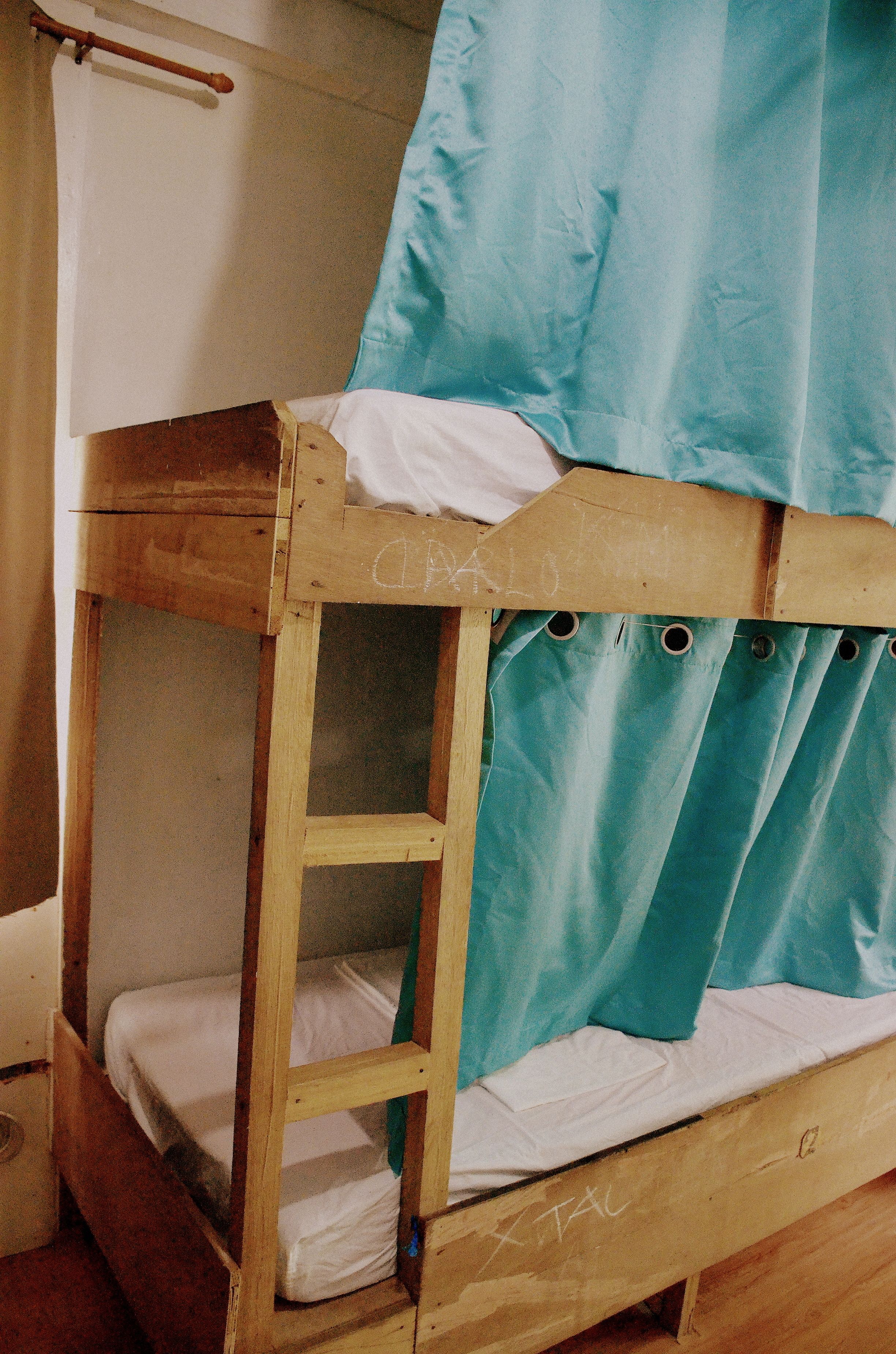 A bunk bed with a wooden frame, a white mattress, and a blue curtain.