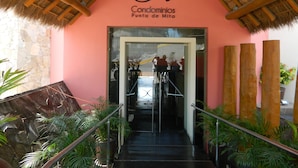 Una entrada de hotel con techo de paja, pared rosa y una escalera que lleva al vestíbulo.