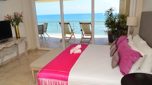 Habitación de hotel con cama, televisión y balcón con sillas y vista al mar.