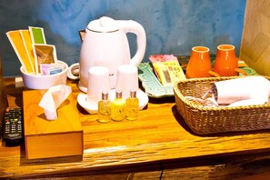 A hotel room's breakfast setup with a kettle, tea cups, a basket, and toiletries.