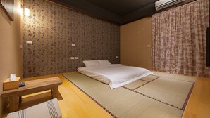 Una habitación japonesa tradicional con suelo de tatami, una cama con ropa blanca, un banco de madera y una pared con papel tapiz estampado.