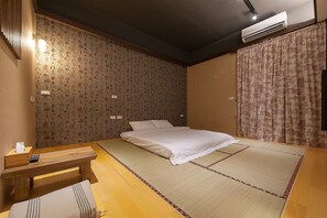 Een traditionele Japanse kamer met tatami vloeren, een bed met witte beddengoed, een houten bank en een wand met behang met een patroon.