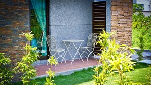 Un patio con una mesa y sillas, rodeado de follaje y un muro de piedra.