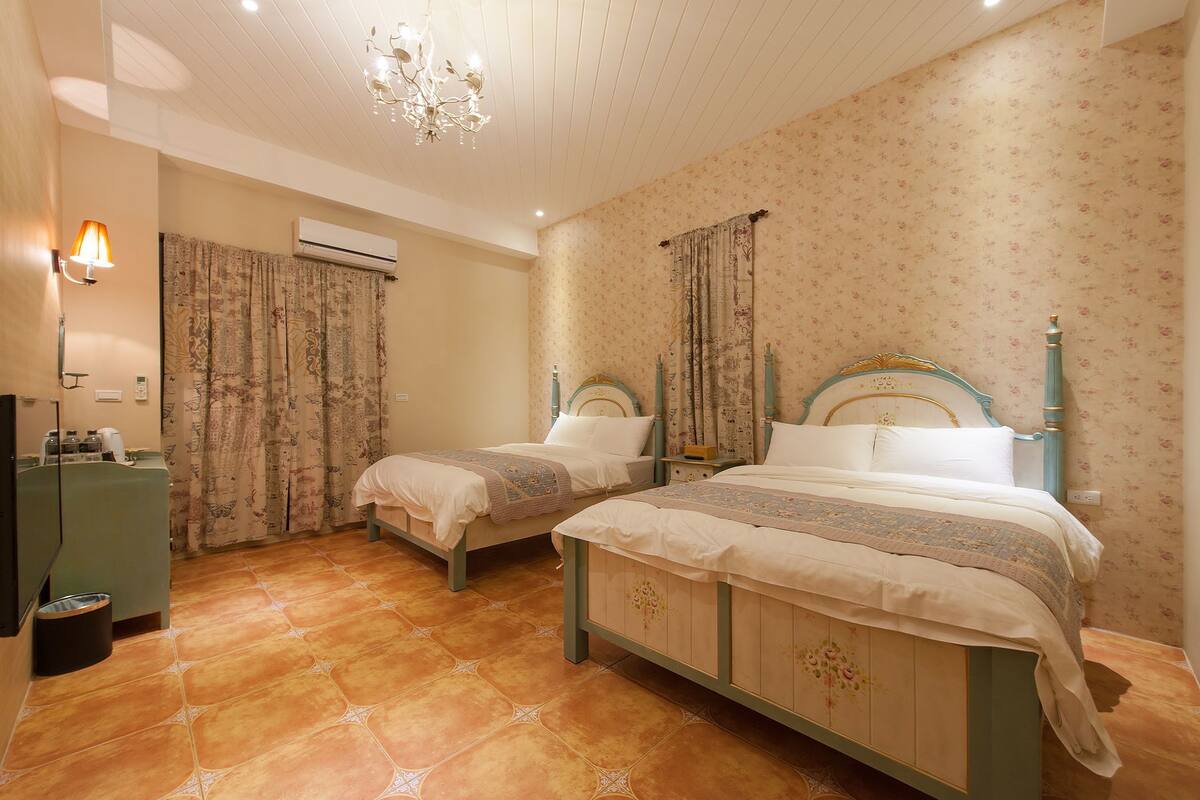 Een slaapkamer met twee bedden, een airconditioner, een kroonluchter en een klein bureau met lamp.