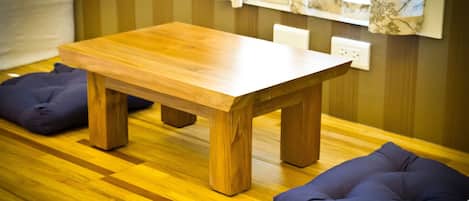 Une table en bois, avec un coussin de chaque côté, posée sur un plancher en bois, le tout devant un mur à rayures.